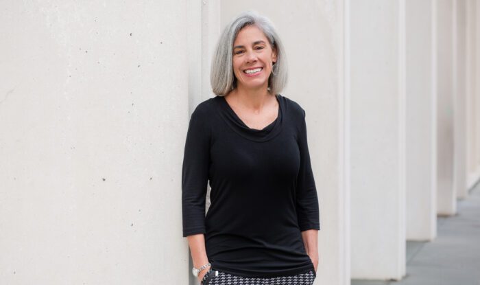 A woman leans up against a white wall