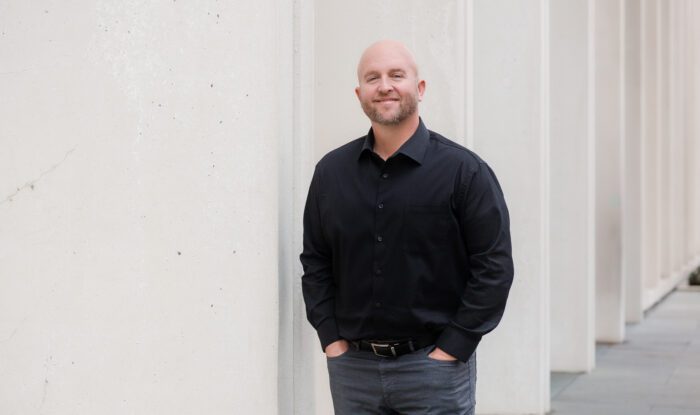 A man leans up against a white wall