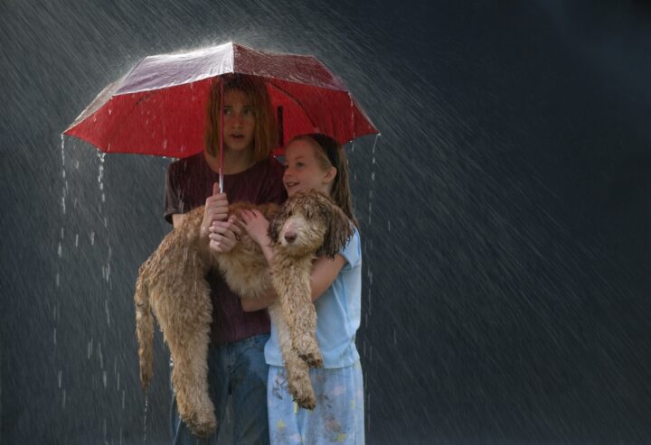 A mother and her daughter hold their dog while standing under an umbrella