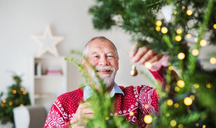 A senior man standing by Christmas tree, holding balls ornaments