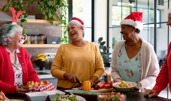 Four happy diverse senior women stand around a table and smile with santa hats on