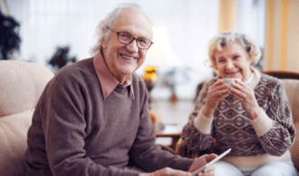 An elderly couple looks at an ipad and smiles