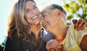 An elderly white woman laughs as her daughter puts her arm around her.