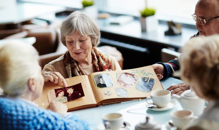 an elderly woman shows photos from a album to her friends
