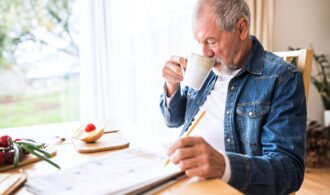 a elderly man takes a sip of his tea while doing a crossword