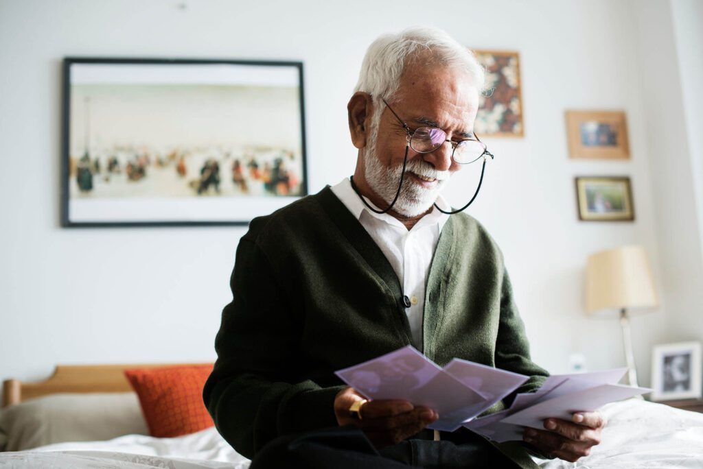 an elderly man with glasses smiles as he checks the mail