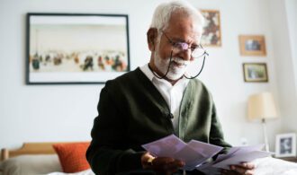 an elderly man with glasses smiles as he checks the mail