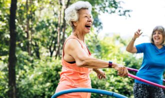 a elderly woman hulahoops outside with a large smile