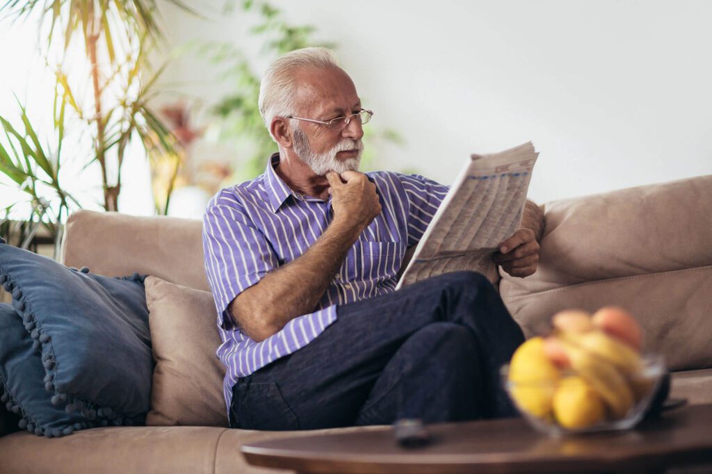 an elderly man reads a newspaper on the couch