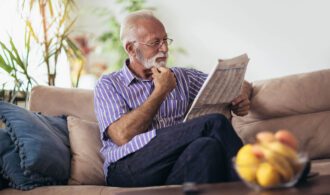 an elderly man reads a newspaper on the couch