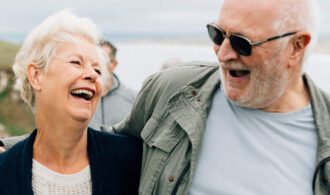 Elderly caregiver laughs with his wife at the beach