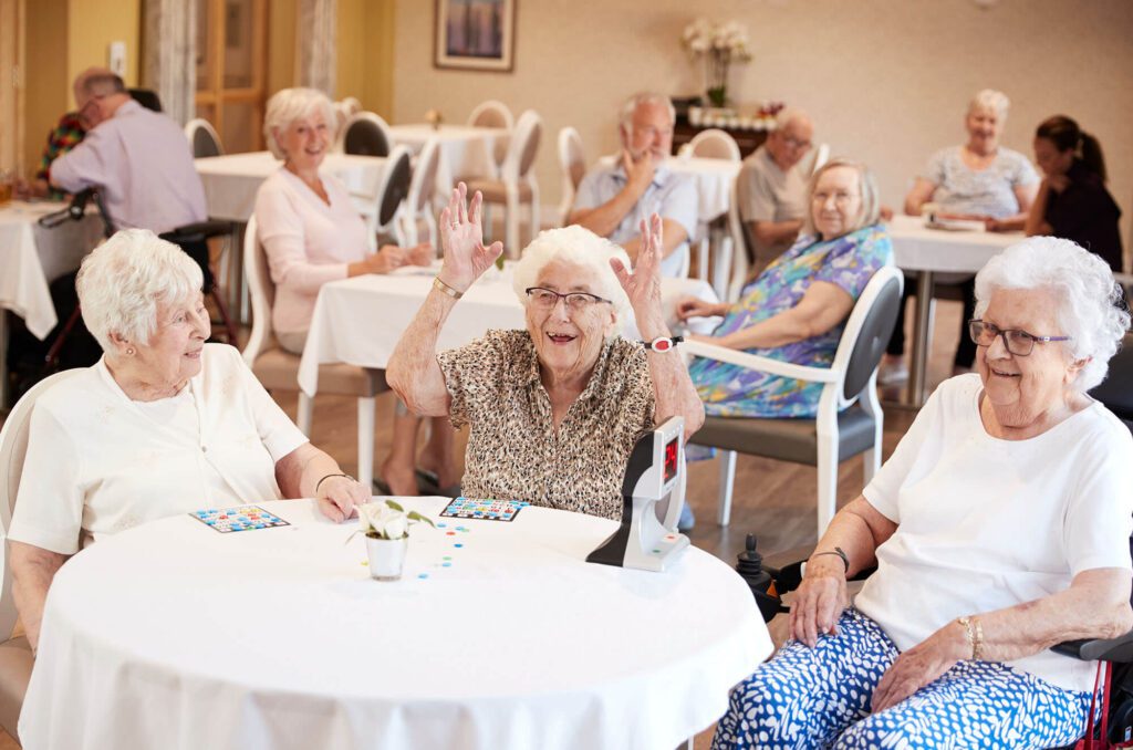 a group of three elderly women play a game while one throw their arms up