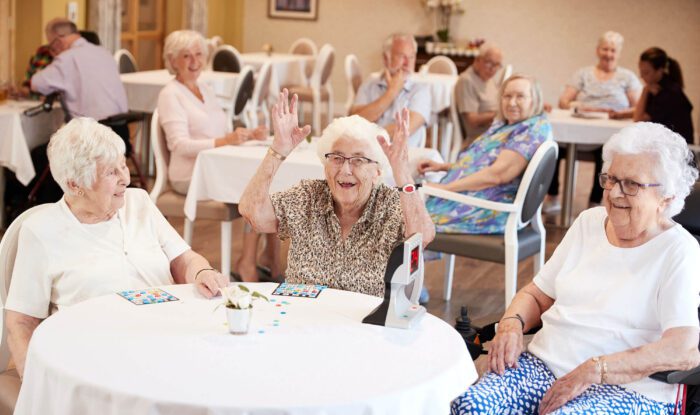 a group of three elderly women play a game while one throw their arms up