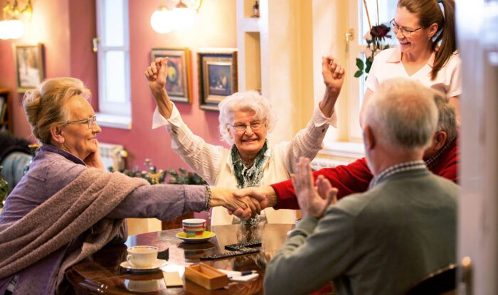 An elderly woman cheers as she wins the game with her friends in assisted living