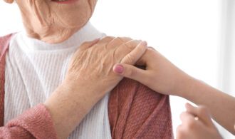 an elderly woman places her hand on top of a caretaker who has put her hand on her shoulder