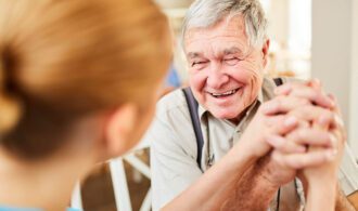 a elderly man holds the hands of a caretaker with a big smile