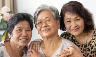 3 relatives stand smiling and hugging in senior living