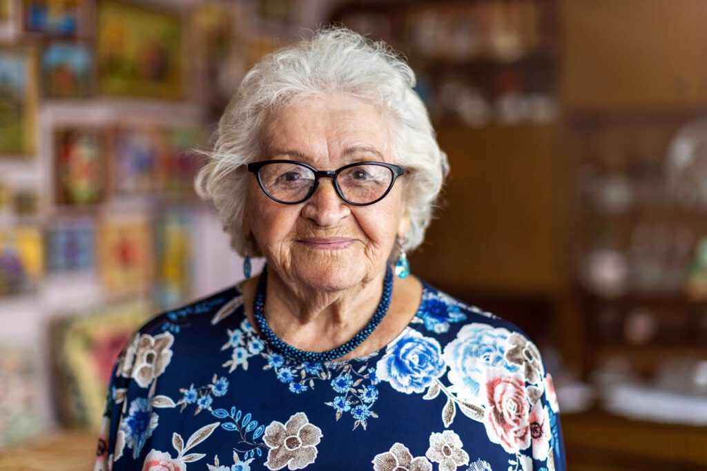 an elderly woman with glasses smiles for the camera