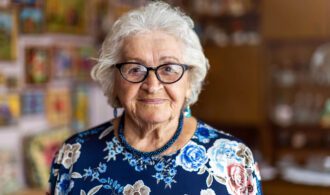 an elderly woman with glasses smiles for the camera