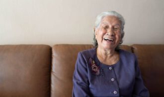 an elderly woman laughs while sitting on the couch