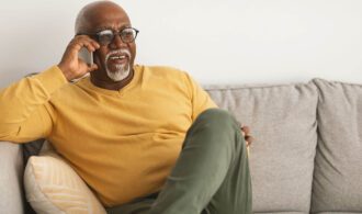 an elderly man sits on a sofa and takes a call
