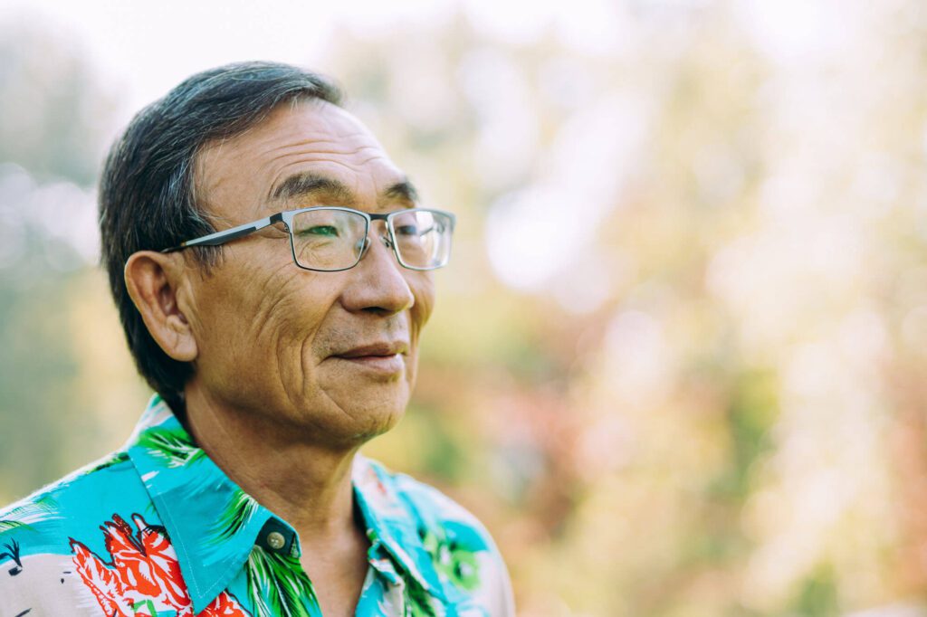an elderly man with glasses and bright shirt smiles outside