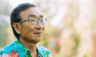 an elderly man with glasses and bright shirt smiles outside