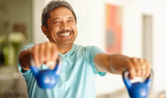 a man manages stress and anxiety with exercise. He has his arms extended lifts two kettle bell weights and smiles
