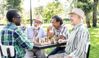 4 elderly men socially engage and play chess in the park