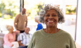 an elderly woman smiles widely with a green sweater in her assisted living community