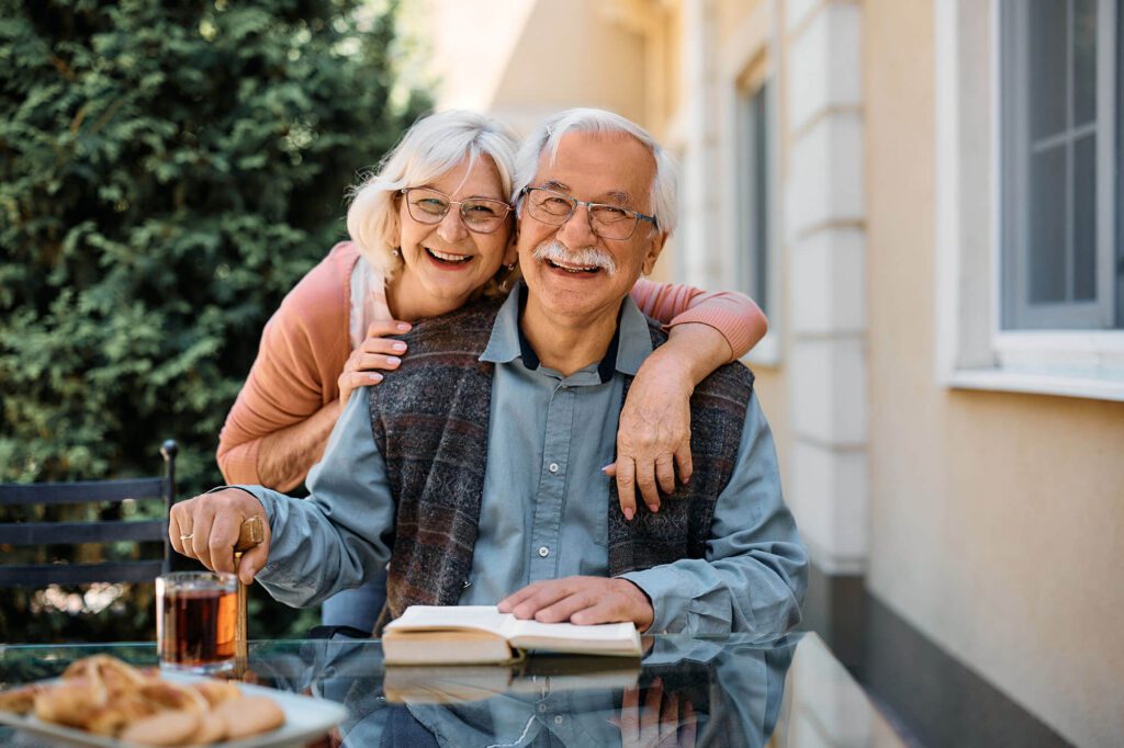 an elderly couple smiles while reading a book