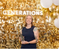 Woman stands in front of a gold backdrop and accepts an award