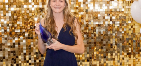 Woman stands in front of a gold backdrop and accepts an award
